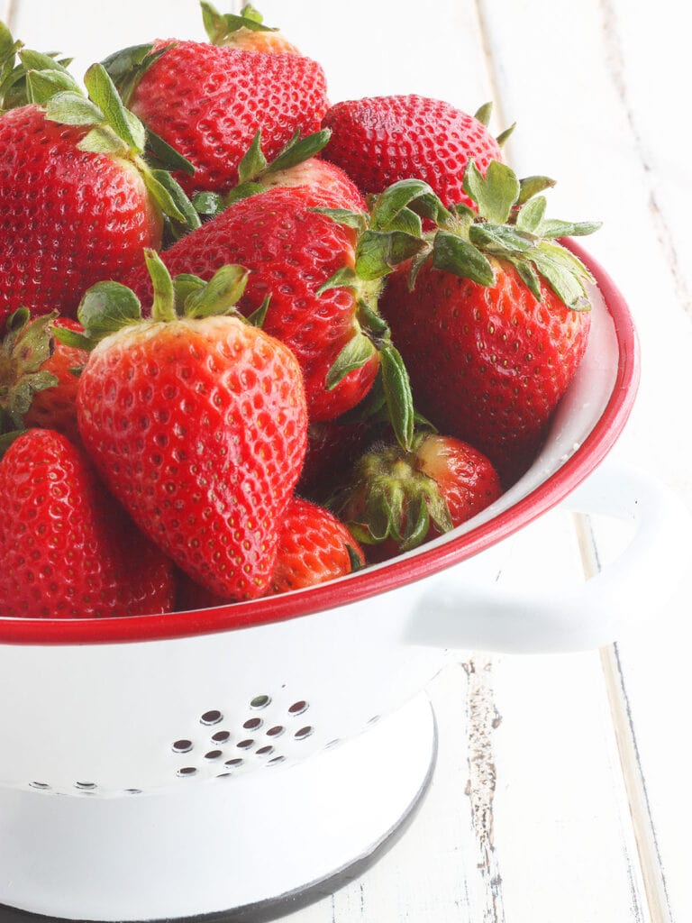 Whole fresh strawberries in a red and white colander.