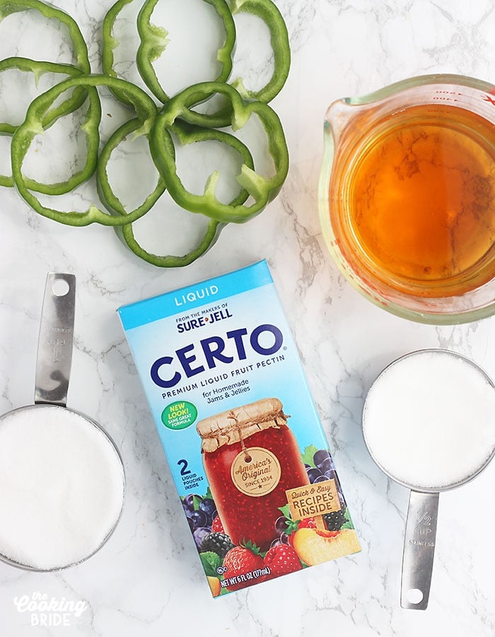 Certo liquid pectin laying on a marble surface surrounded by pepper slices, vinegar, and sugar