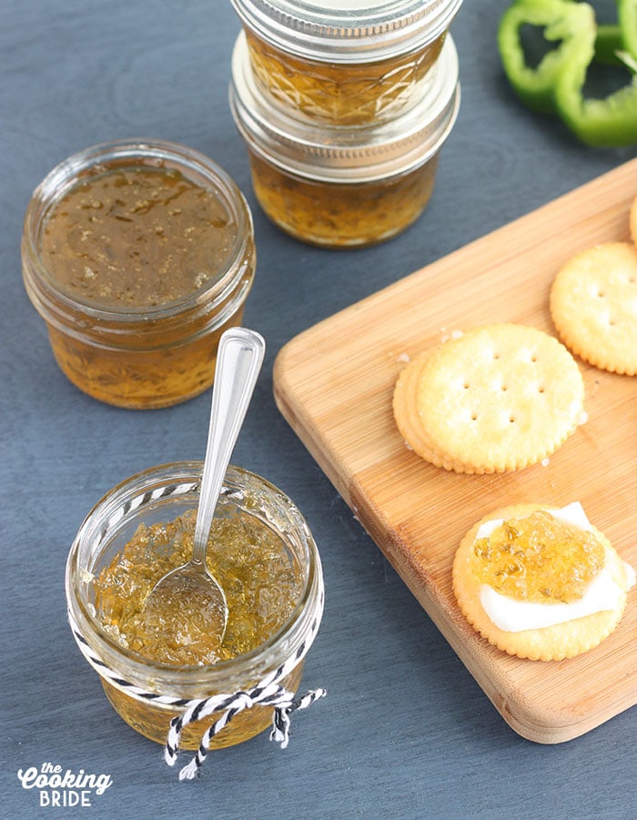 small jelly jar of pepper jelly with crackers, fresh pepper slices and jelly jars in the background