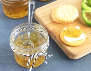 small jelly jar of pepper jelly with crackers, fresh pepper slices and jelly jars in the background