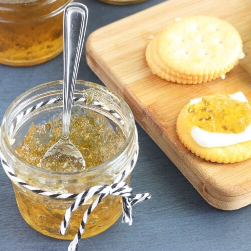 small jelly jar of pepper jelly with crackers, fresh pepper slices and jelly jars in the background