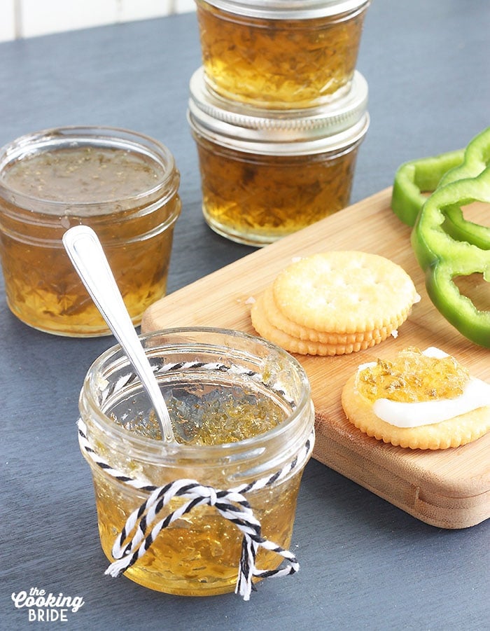 small jelly jar of pepper jelly with crackers, fresh pepper slices and jelly jars in the background