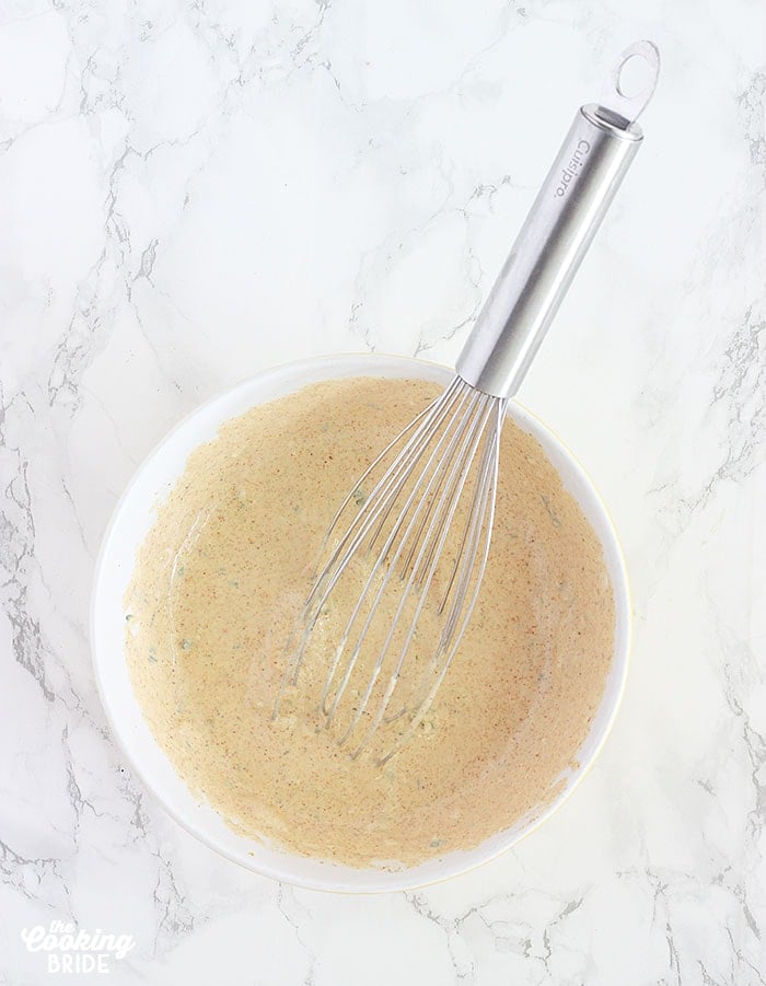 metal whisk resting in a bowl of whipped remoulade sauce