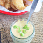 mason jar of remoulade sauce sprinkled with green onions and fried catfish in the background