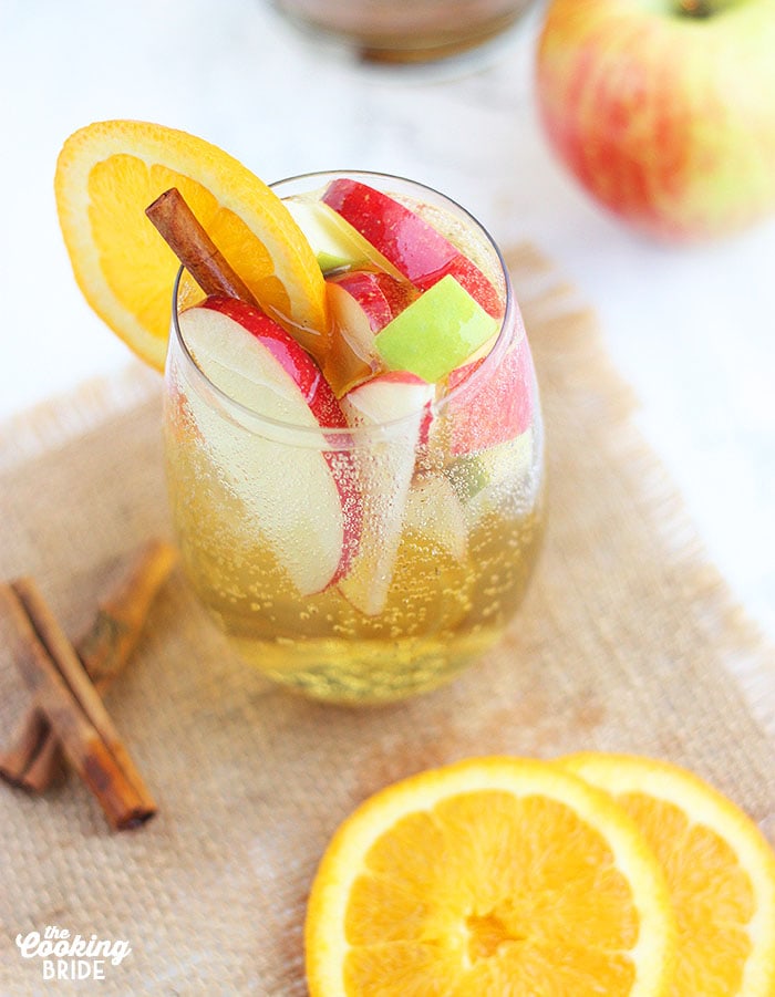 overhead shot of clear glass of apple cider sangria filled with apple slices and garnished with an orange and cinnamon stick