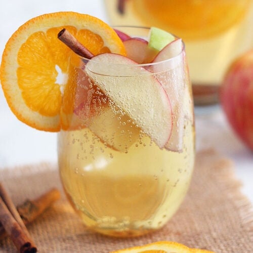 clear glass of apple cider sangria filled with apple slices and garnished with an orange and cinnamon stick