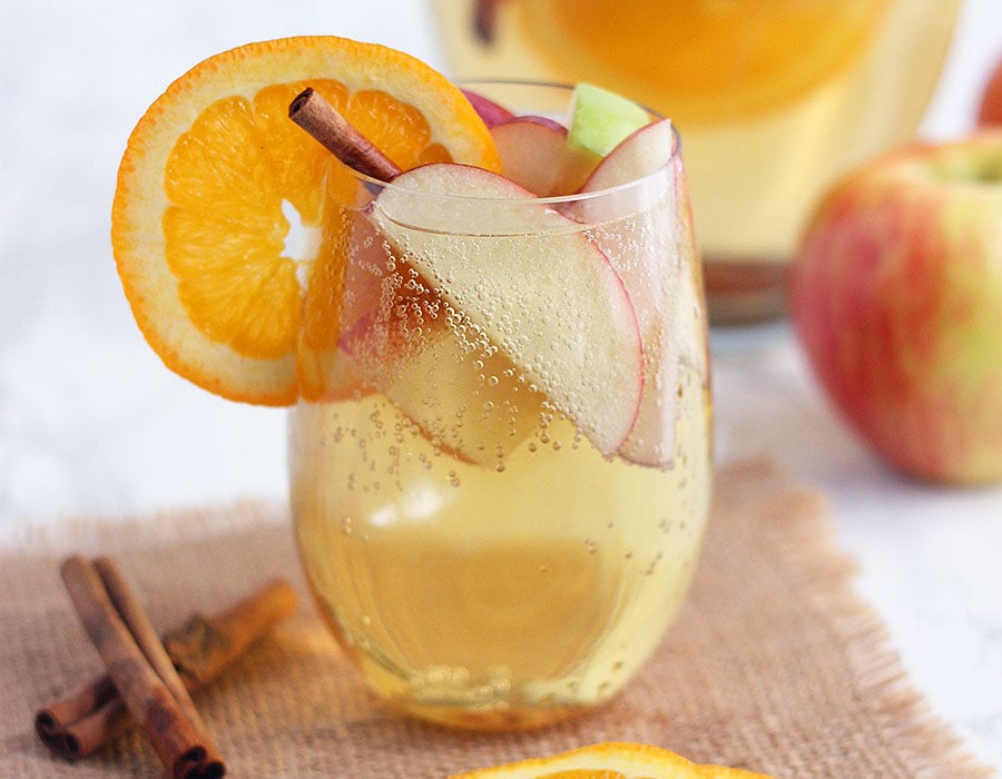 clear glass of apple cider sangria filled with apple slices and garnished with an orange and cinnamon stick
