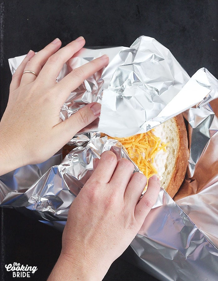 pair of hands wrapping the dip in aluminum foil