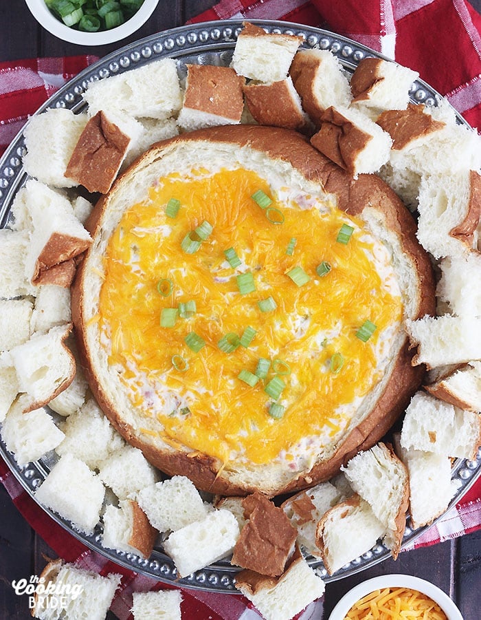 bread bowl filled with baked sin dip on a silver platter surrounded by cubed bread