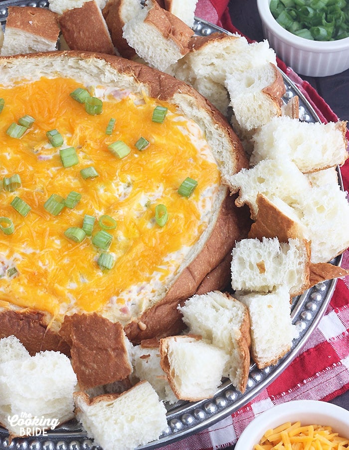 bread bowl filled with baked sin dip on a silver platter surrounded by cubed bread