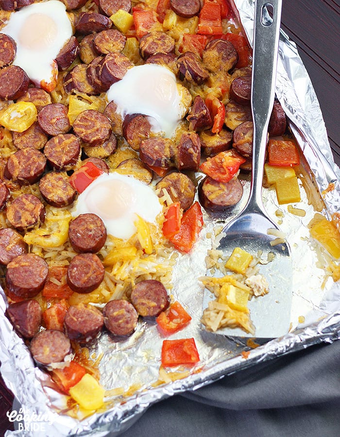 smoked sausage with veggies on a foil line baking sheet and a metal spatula.