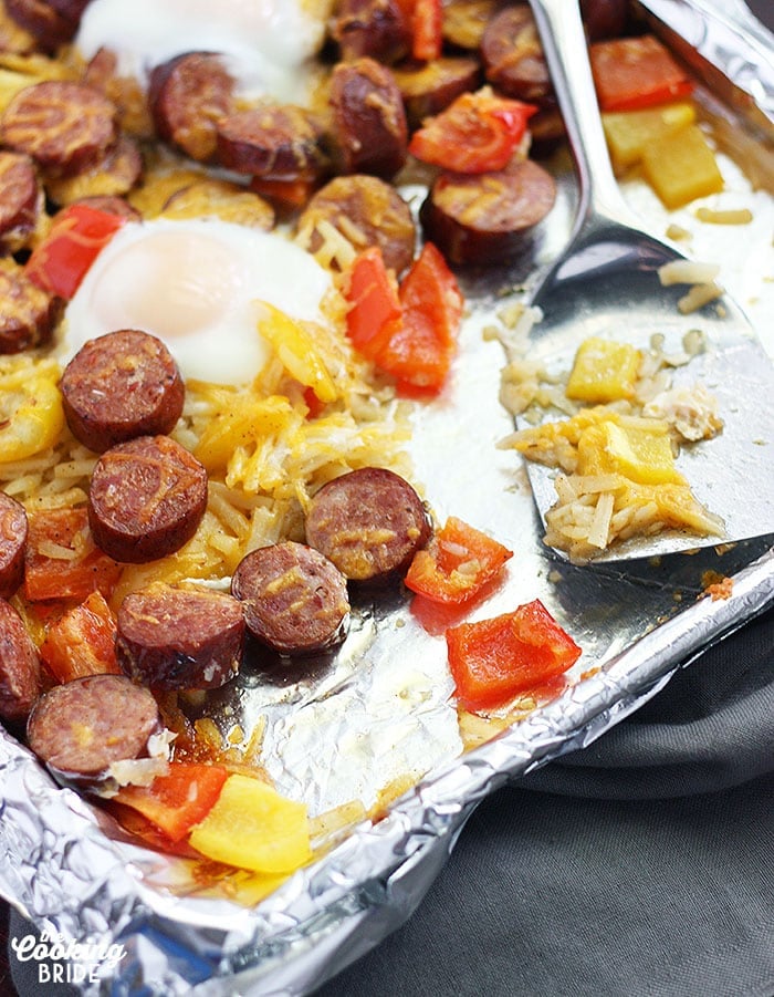 smoked sausage with veggies on a foil line baking sheet and a metal spatula.