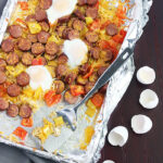 smoked sausage with veggies on a foil line baking sheet and a metal spatula. Cracked egg shells to the side.