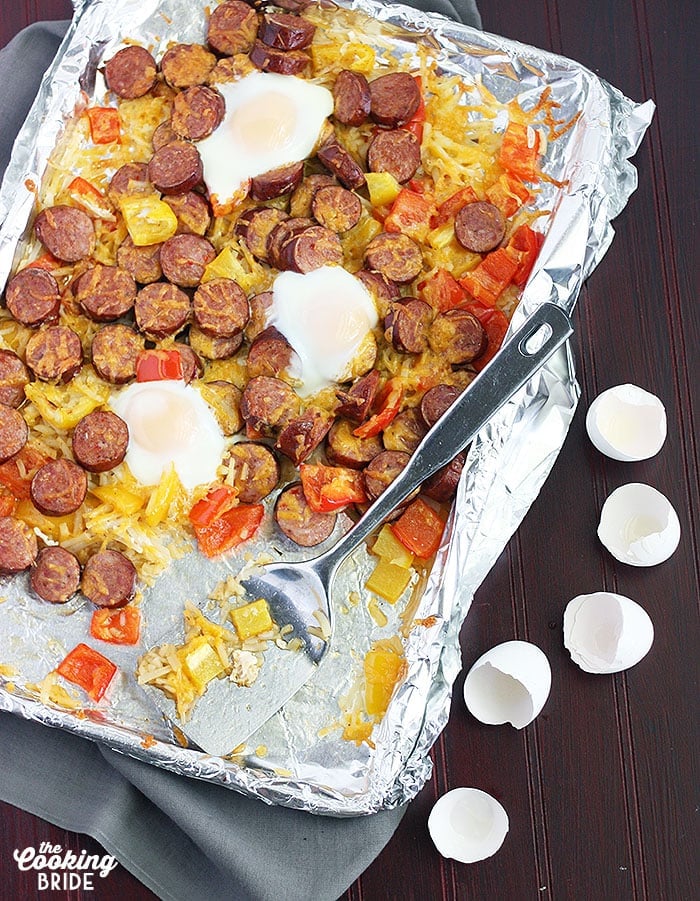 smoked sausage with veggies on a foil line baking sheet and a metal spatula. Cracked egg shells to the side.