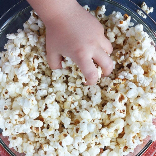 little hand reaching into a glass bowl full of homemade kettle corn