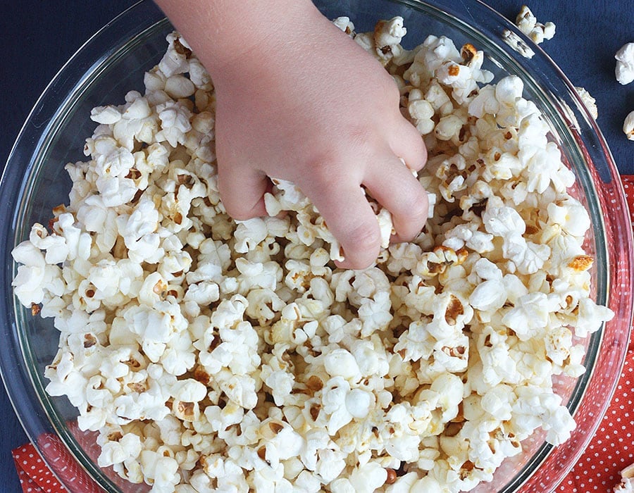 little hand reaching into a glass bowl full of homemade kettle corn