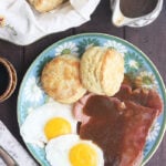 plate of sunny side up eggs, biscuits and country ham covered in red eye gravy