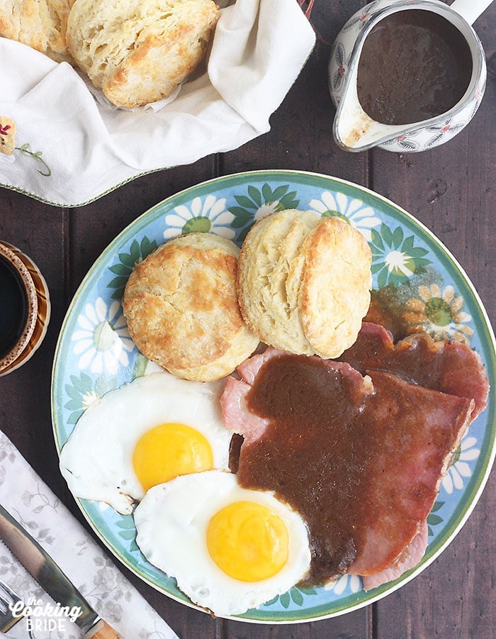 plate of sunny side up eggs, biscuits and country ham covered in red eye gravy