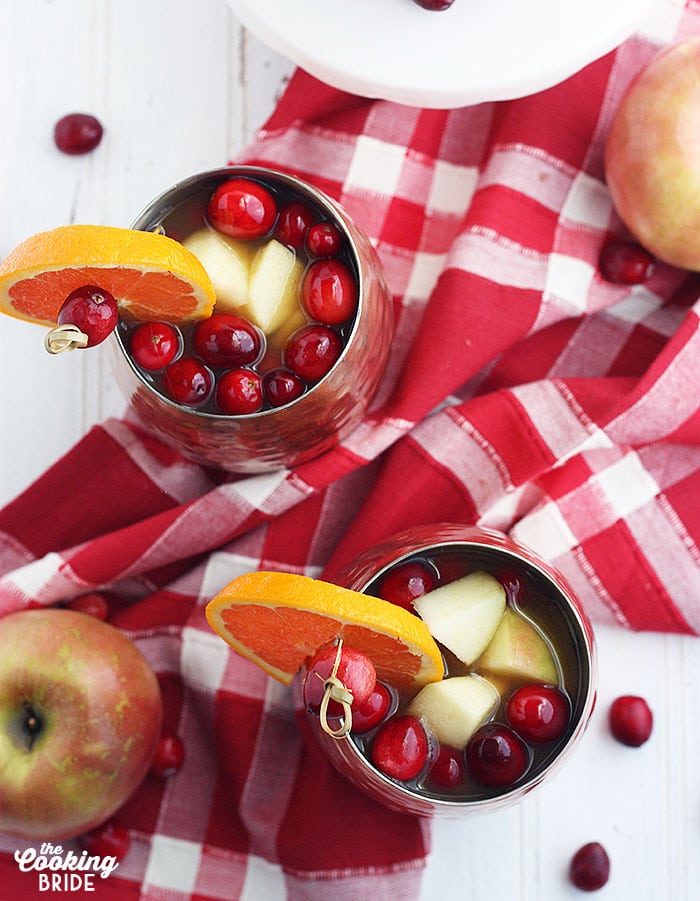 over heat shot of a glass of apple cider garnished with apples, cranberries and orange slices