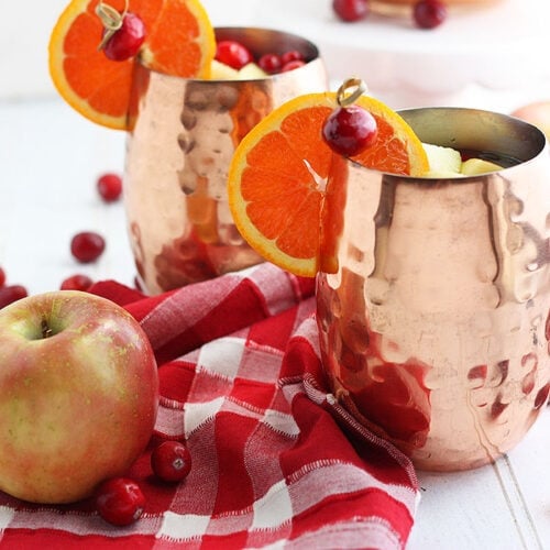 two copper mule cups of spiced apple cider against a red plaid napkin
