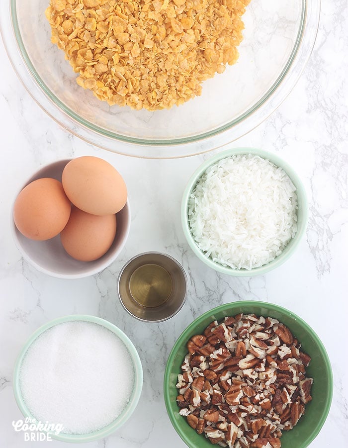 ingredients for cornflake cookies including cornflakes, eggs, coconut, vanilla, sugar and chopped pecans