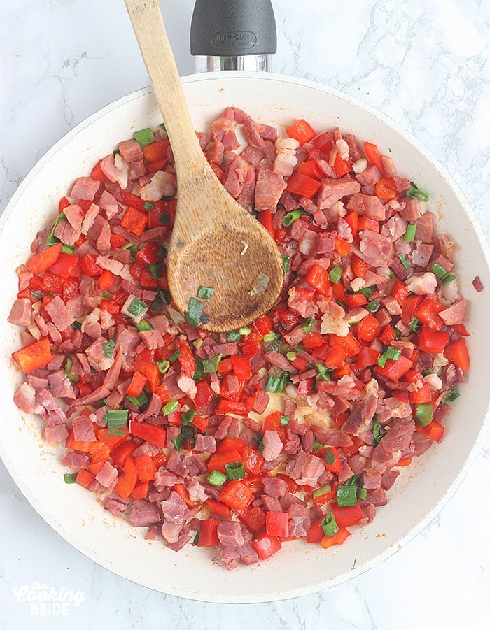 sauteed ham, red bell peppers and green onions in a skillet with a wooden spoon