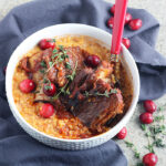 short ribs nestled in corn grits garnished with fresh cranberries and thyme in a white bowl