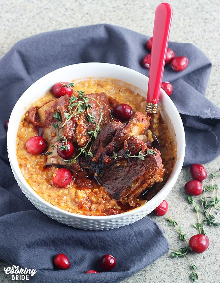short ribs nestled in corn grits garnished with fresh cranberries and thyme in a white bowl