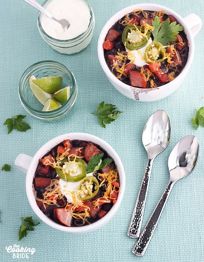 two white mugs full of black bean soup garnished with sour cream, cheese and jalapenos