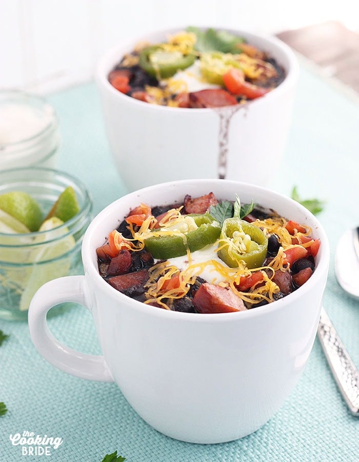 two white mugs full of black bean soup garnished with sour cream, cheese and jalapenos