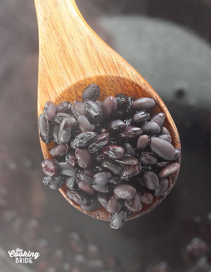 close up of soaked black beans on a wooden spoon