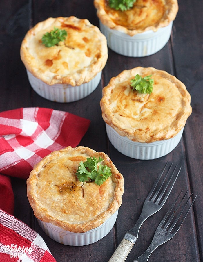 three baked crawfish pies on a wooden background with a red plaid napkin