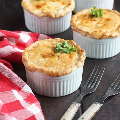three baked crawfish pies on a wooden background with a red plaid napkin
