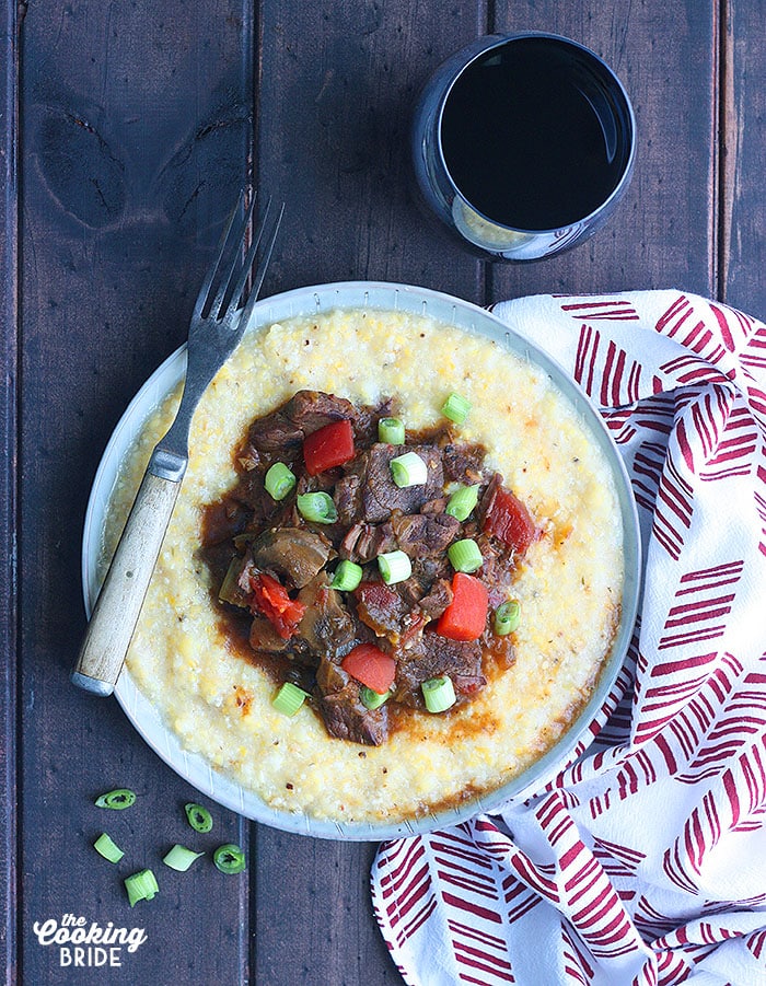 grillades and grits on a gray plate with a red and white napkin and a glass of red wine