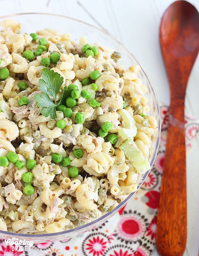 close up shot of tuna macaroni salad in a clear serving bowl with a wooden serving spoon on the side