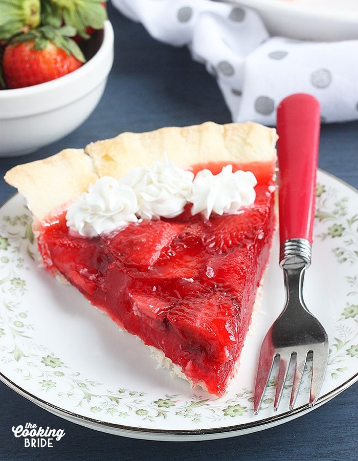 one slice of fresh strawberry pie topped with whipped cream on a floral plate on a blue background