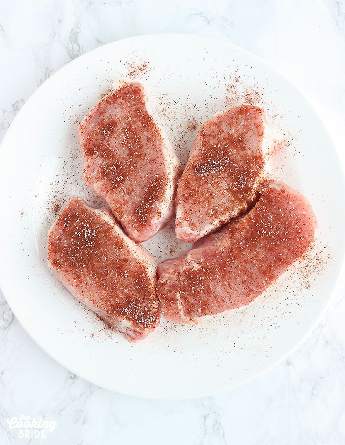 uncooked pork chops sprinkled with seasoning on a white plate