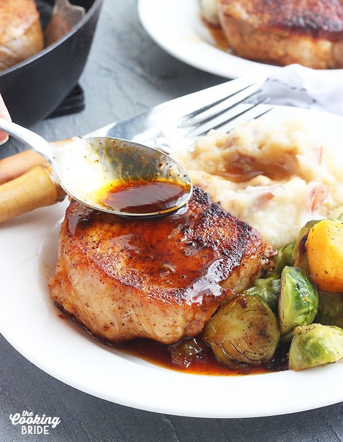 spooning maple glaze over the top of a plated pork chops