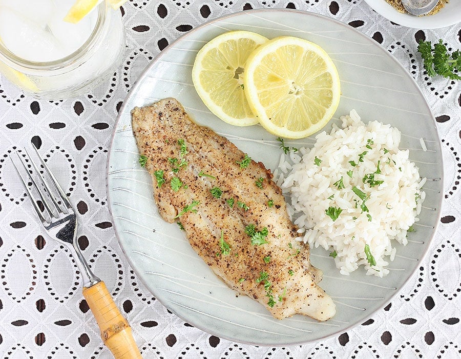 lemon pepper catfish fillet with rice an lemon slices on a gray plate