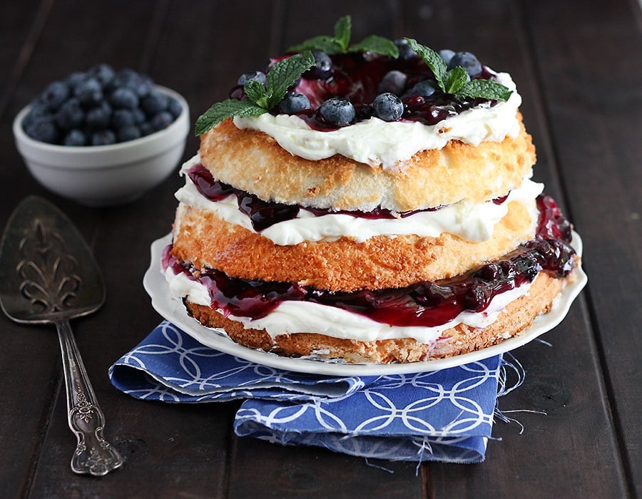 blueberry icebox cake garnished with mint leaves on a white plate served on a blue and white napkin with a silver cake server and a small bowl of blueberries in the background