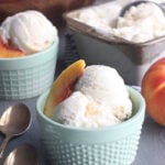 two bowls of homemade peach ice cream with a metal container of ice cream and a bowl of peaches in the background