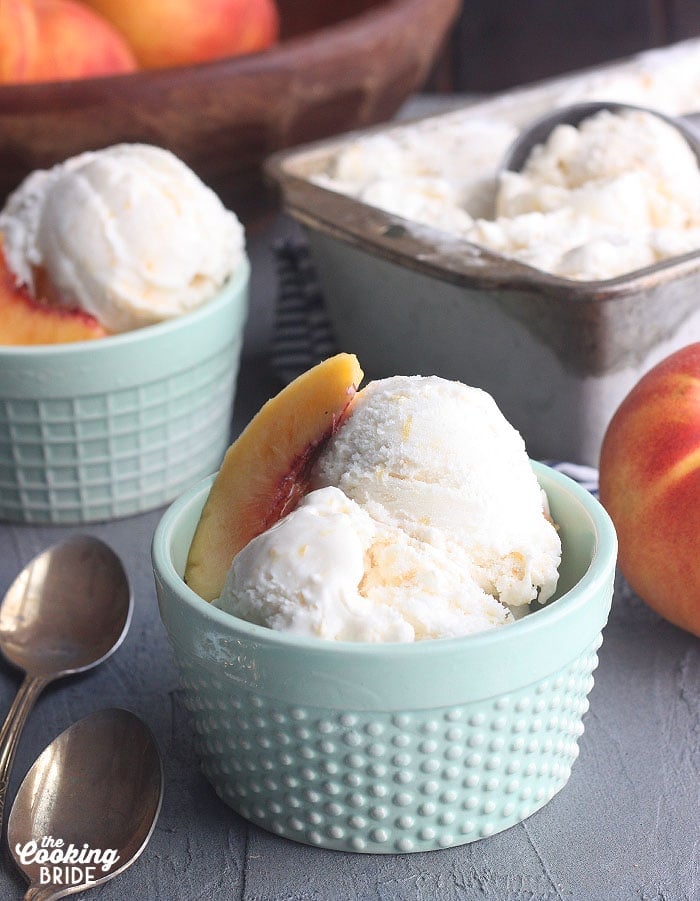 two bowls of homemade peach ice cream with a metal container of ice cream and a bowl of peaches in the background