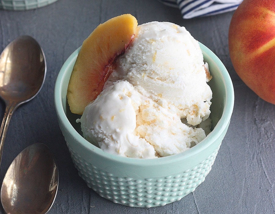 homemade peach ice cream in a small blue bowl with spoons to the side
