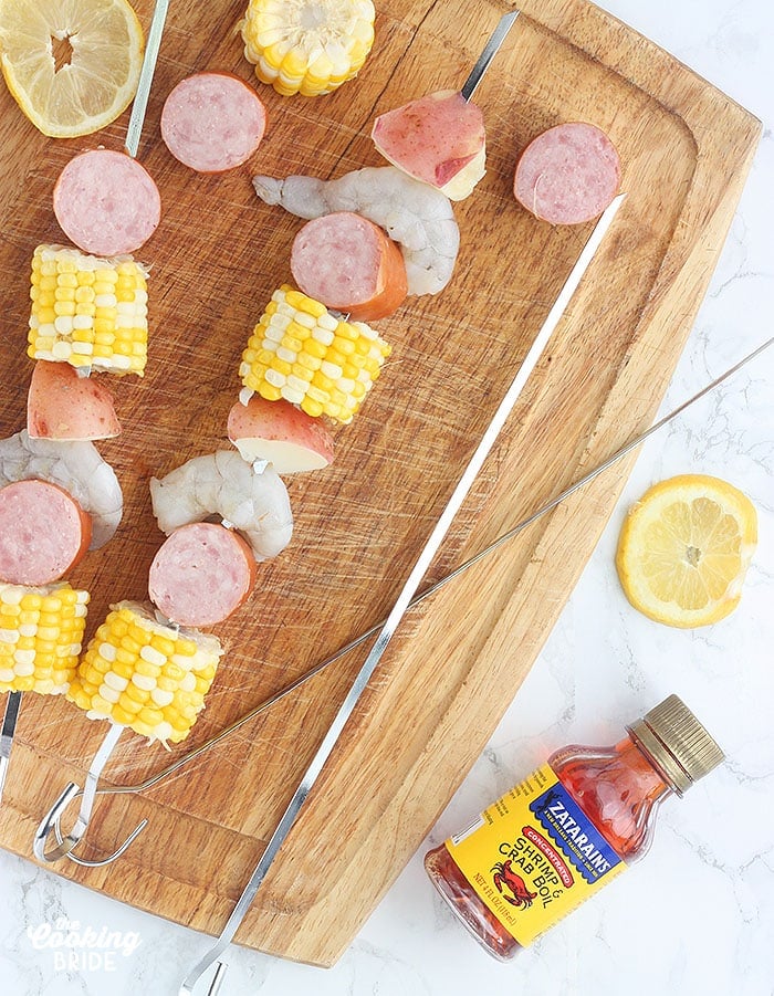 threading the shrimp, corn, potatoes and sausage onto metal skewers