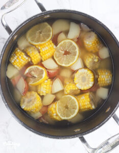 corn, potatoes and lemon slices soaking in a large stock pot of water