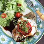 Caprese baked catfish fillet and a simple salad on a blue and green floral plate with a fork on the side