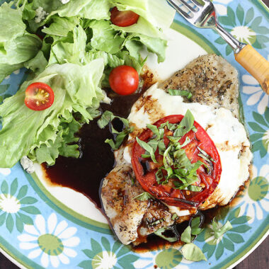 Caprese baked catfish fillet and a simple salad on a blue and green floral plate with a fork on the side