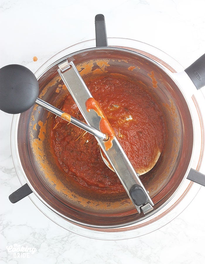 straining the cooked tomato soup through a food mill