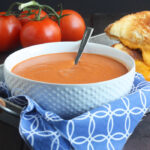bowl of cream of tomato soup sitting on a tray with a blue napkin underneath