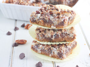 Three cut Hello Dolly bars stacked on top of each other on a white wooden table